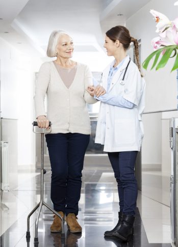 Doctor Assisting Senior Woman With Cane In Rehabilitation Center